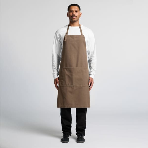A canvas apron in brown worn by a standing individual, featuring a front pocket and ties at the neck and waist.