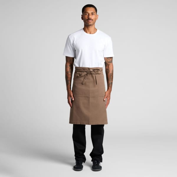 A person wearing a brown canvas half apron over a white shirt, standing against a plain background.