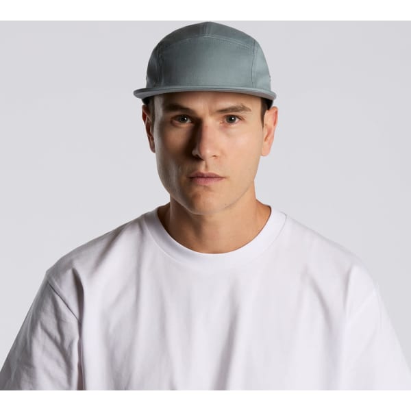 A five-panel cap in grey being worn by a model with a plain white t-shirt, featuring a logo on the front.