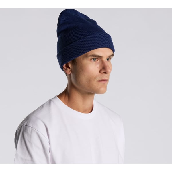 A navy cuff beanie is worn by a model, paired with a plain white t-shirt. The beanie features a logo.