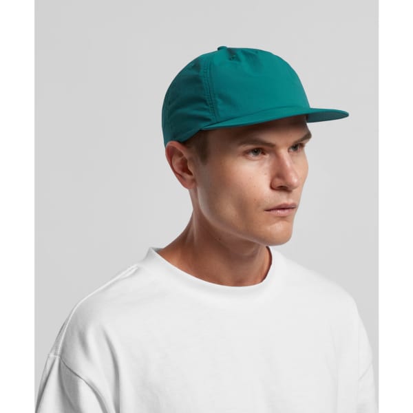 A teal cap with a flat brim, featuring a logo, worn by a male model in a white shirt.