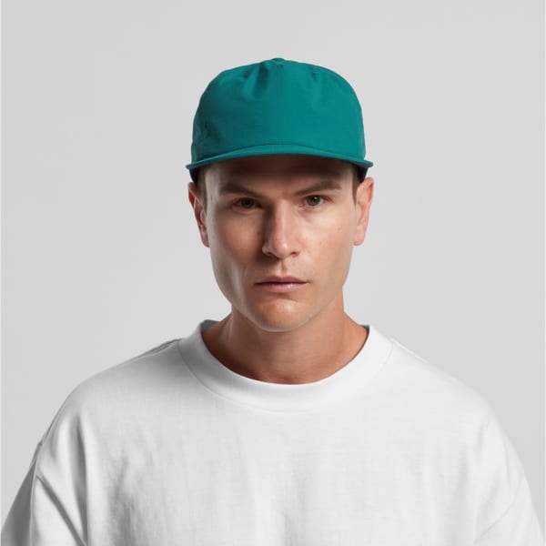 A teal cap with a flat brim and a fitted design, worn by a model in a white sweatshirt.