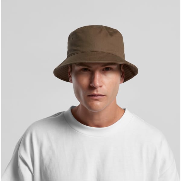 A brown bucket hat with a wide brim, worn by a model in a white t-shirt. The hat features a logo.