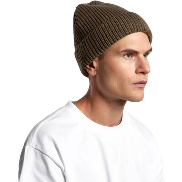 A ribbed olive green beanie is worn by a model, featuring a snug fit. The product has a logo.