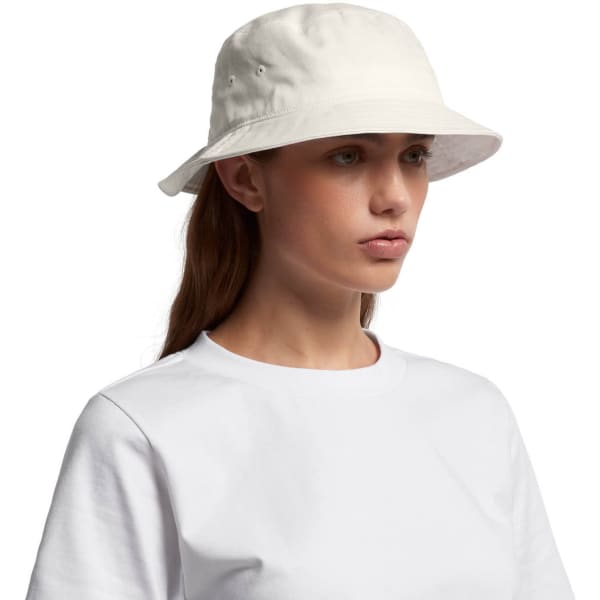 A white bucket hat is featured, made of soft fabric with a brim and eyelet vents, worn by a model.