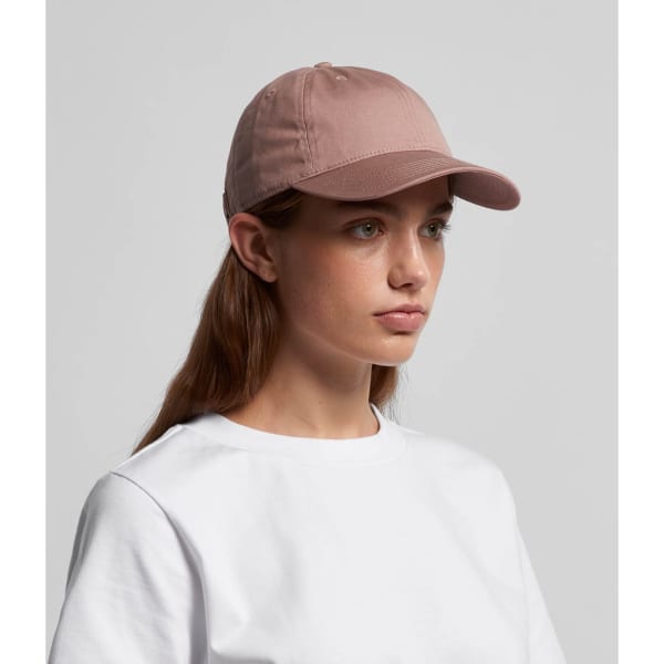 A cap in a soft pink colour, featuring a curved brim and a subtle logo, worn by a young woman.