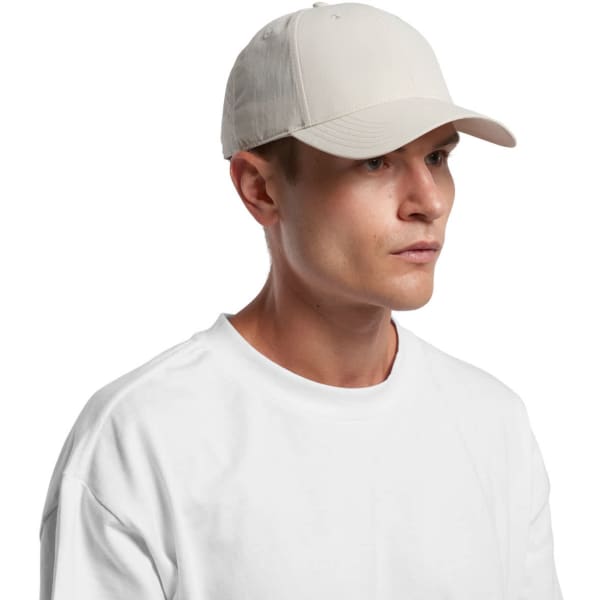 A plain cream-coloured Nylon cap worn by a model, featuring a curved brim and a logo.