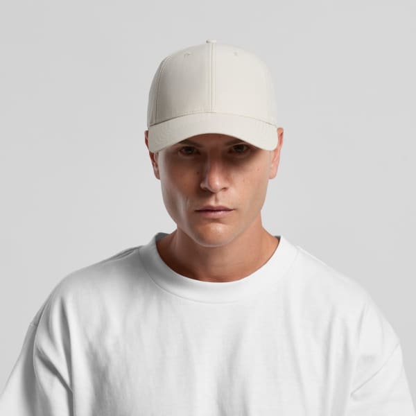 A light beige nylon cap displayed on a model wearing a white sweatshirt. The cap features a logo.