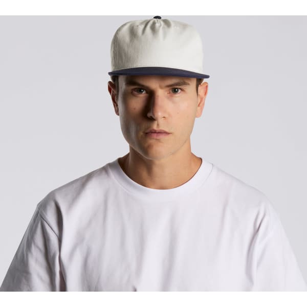 A two-tone cap featuring a cream body and navy peak, displayed on a model wearing a white t-shirt.