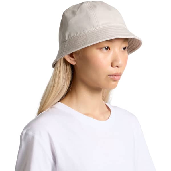 A bucket hat in a light beige colour, featuring a logo, displayed on a model with long hair.