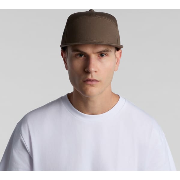 A brown 7-panel cap features a structured design and a logo on the front, worn by a model in a white T-shirt.