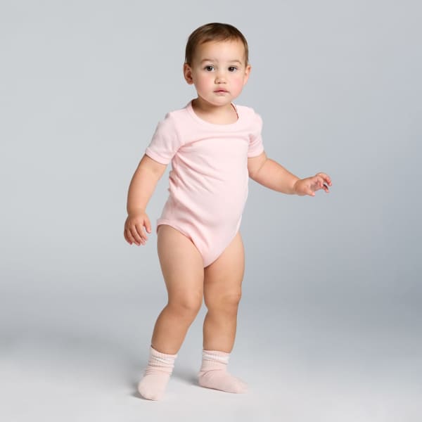 A pink organic infant one-piece with short sleeves, featuring a logo, worn by a toddler standing.