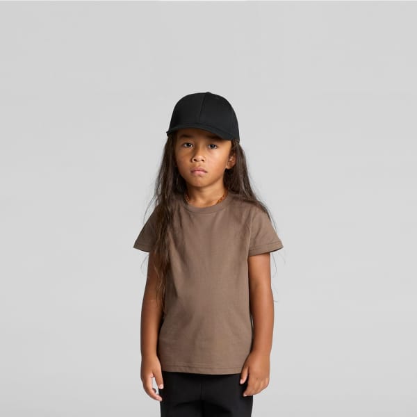 A child wearing a brown staple tee and a black cap, standing against a plain grey background.