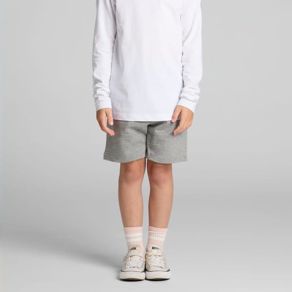 Kids grey stadium shorts displayed on a child wearing a long-sleeve white shirt and light-coloured shoes.