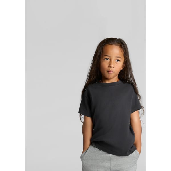 A child wearing a black heavy faded tee, with long hair and hands in pockets, set against a neutral background.