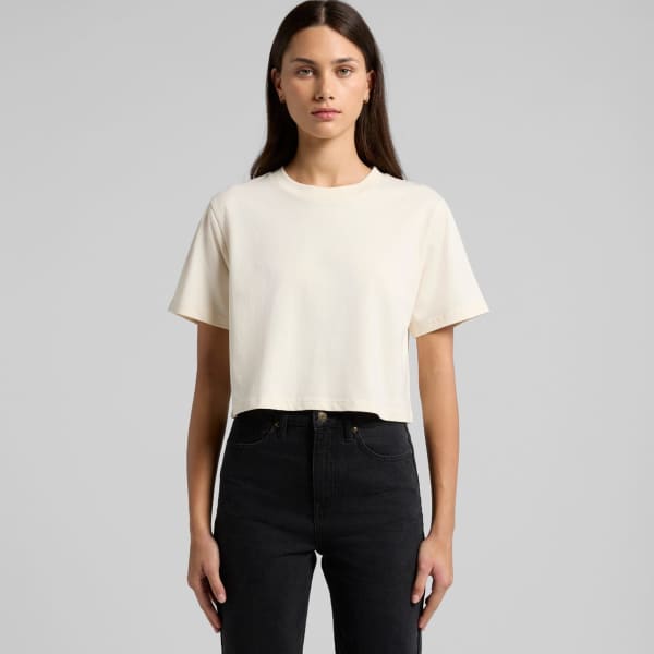 A cropped cream T-shirt with short sleeves, displayed on a model wearing black jeans. The shirt has a logo.