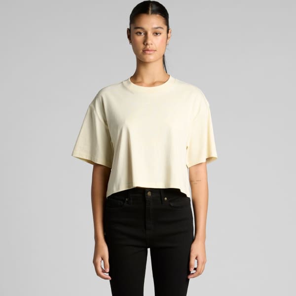 A cropped tee in a soft yellow colour, featuring short sleeves and a loose fit. The model wears black pants and stands against a plain background.