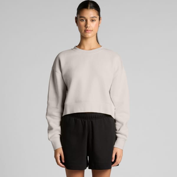 A light grey cropped jumper is displayed, paired with black shorts. The jumper has a relaxed fit and features a branding logo.