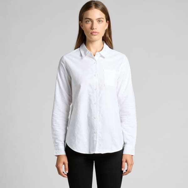A white button-up shirt with a front pocket, featuring a classic collar and long sleeves. The model stands confidently.