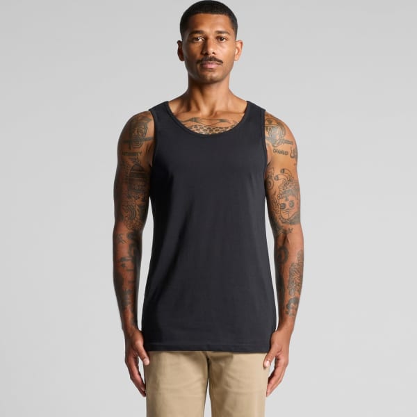 A man with tattoos wearing a plain black singlet against a neutral background. The singlet has a logo.
