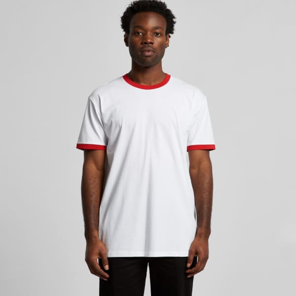 A man stands wearing a white T-shirt with red sleeves and collar, featuring a logo on the chest.