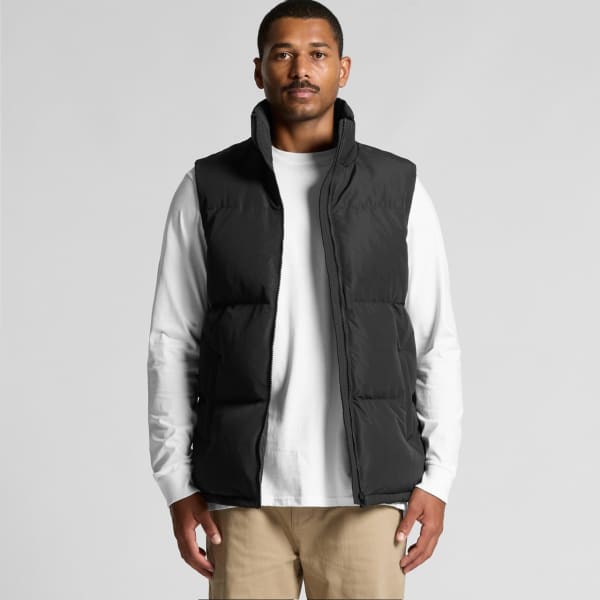 A black puffer vest is worn by a model over a white long-sleeve shirt, set against a neutral background.