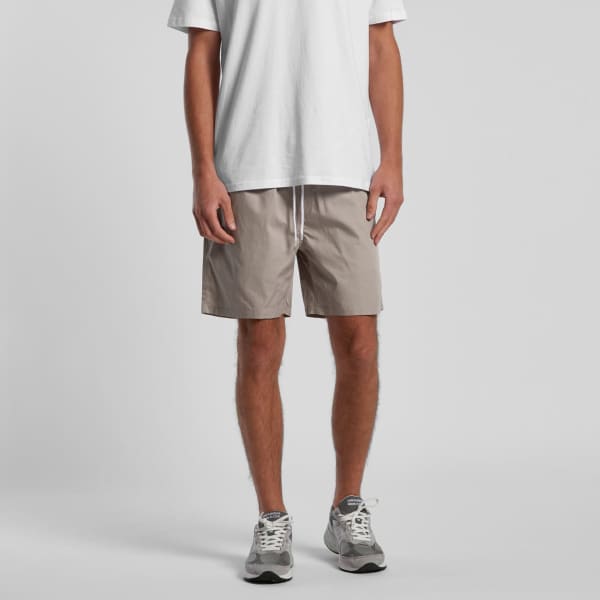 A pair of beige beach shorts, 17 inches long, worn with a white t-shirt and grey sneakers. The shorts feature a drawstring.