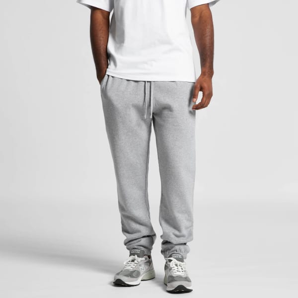 A person wearing grey track pants, paired with a white t-shirt and grey sneakers, standing against a neutral background.