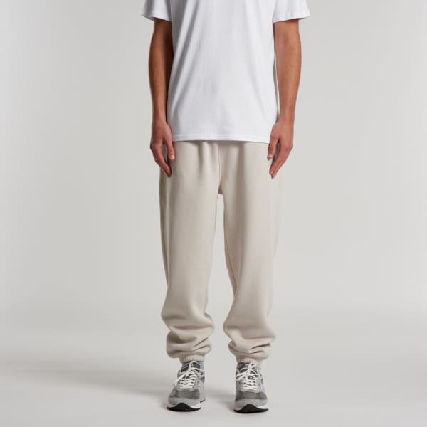 Relax Track Pants in light beige, made from soft fabric, feature an elastic waistband. Model stands in a neutral setting.
