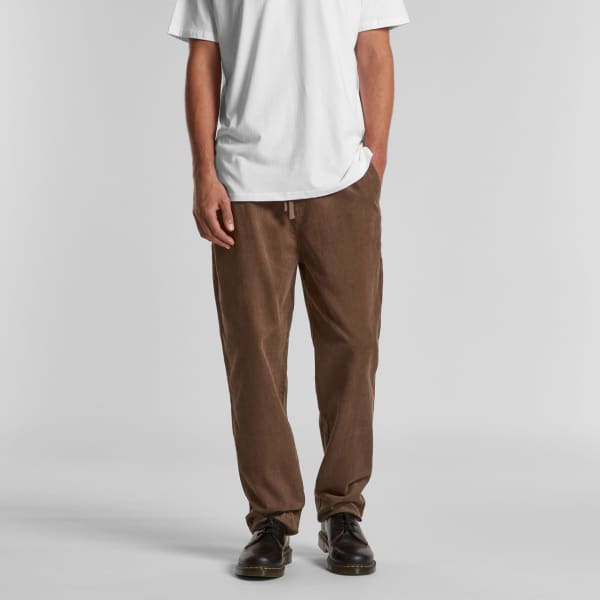 Cord pants in a brown hue, featuring a relaxed fit, with a drawstring waistband and pockets. Styled with a white t-shirt.