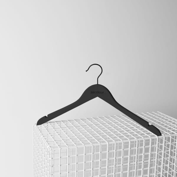 A black clothing hanger with a curved design, placed on a white wire display shelf.