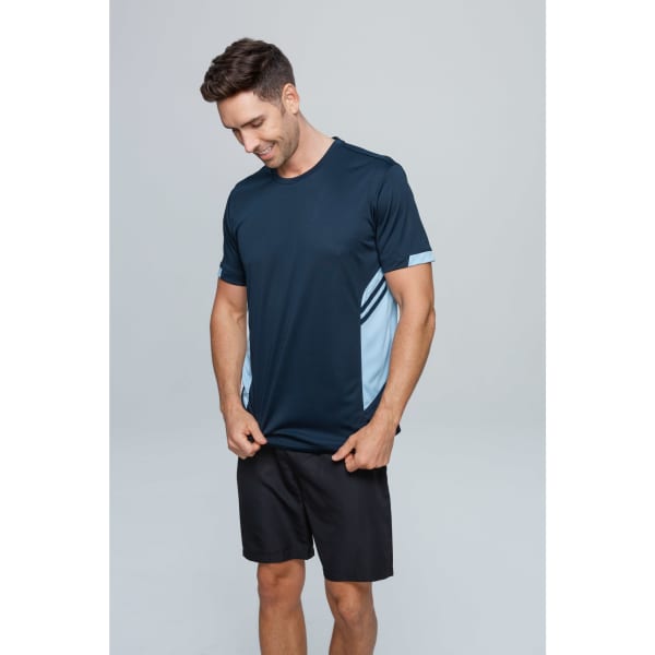 A man in a navy T-shirt with light blue accents stands against a neutral background, wearing black shorts.
