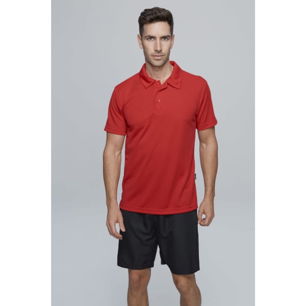 A model wearing a red polo shirt and black shorts, posing against a plain grey background. The polo features a logo.