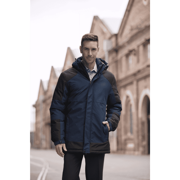 A man wearing a navy and black jacket with a hood, featuring a logo, stands in an urban setting.