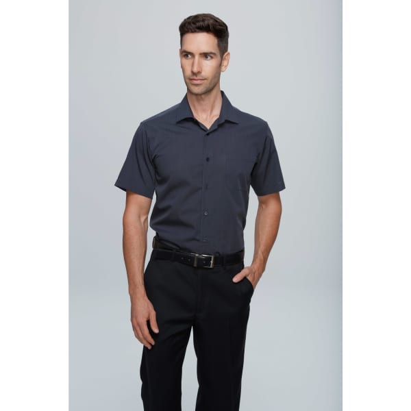 A short sleeve men's button-up shirt in navy blue, featuring a simple design and a small pocket, with a model wearing black trousers.