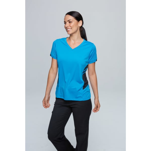 A woman wearing a blue sports tee with black accents and black pants, smiling against a plain background.
