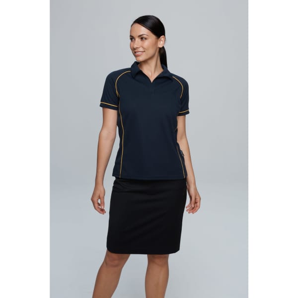 A woman in a navy polo shirt with yellow piping, paired with a black skirt, stands against a plain background.