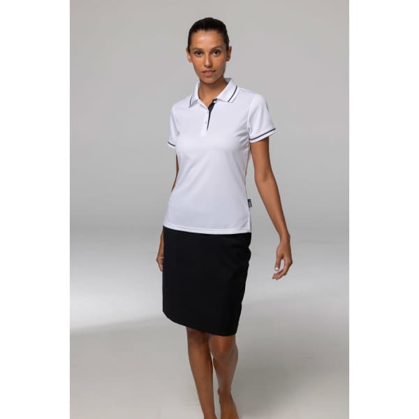 A woman wearing a white polo shirt with black trim and a black skirt, standing in a neutral setting.