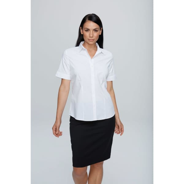 A short-sleeve white button-up shirt displayed on a model, paired with a black skirt. The shirt features a logo.