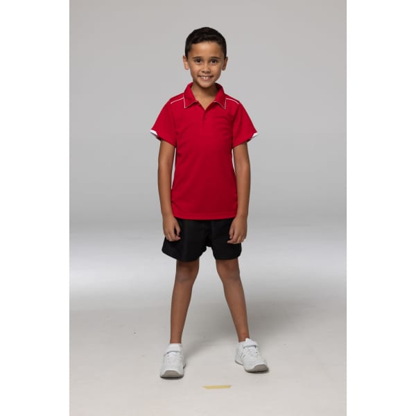 A child wearing a red polo shirt with white accents and black shorts, standing with a neutral background.