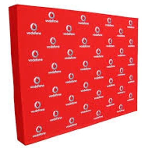 A promotional media wall in bright red, featuring a repeating logo pattern.