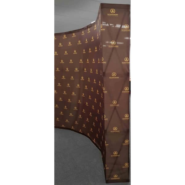 A brown promotional media wall featuring a repeating logo pattern in gold.