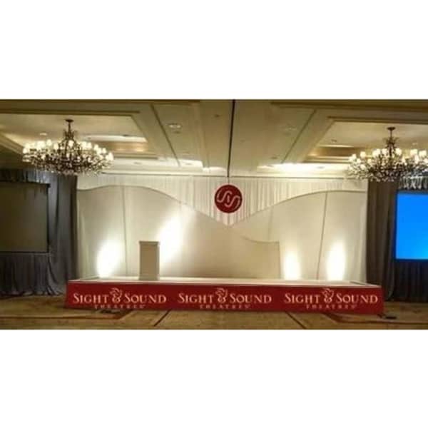 A polyester stage skirt in grey, set against a backdrop with a logo and elegant lighting.