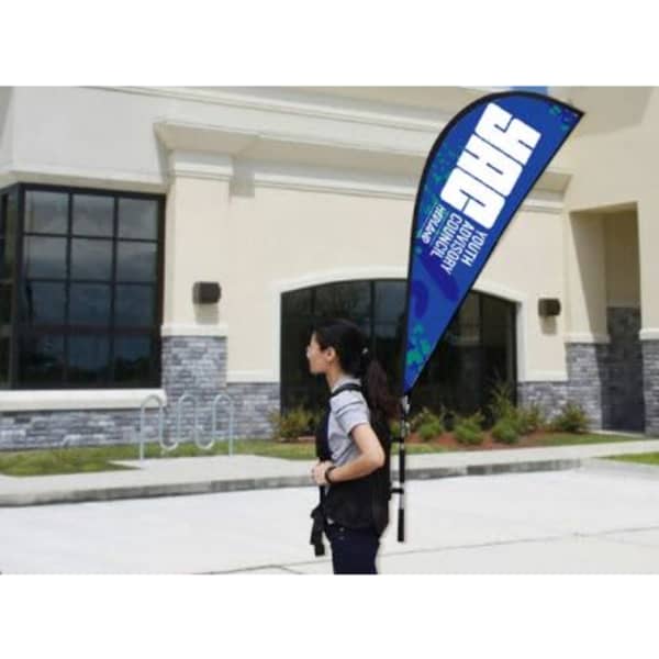 A person carrying a blue teardrop banner backpack with a logo outside a building.