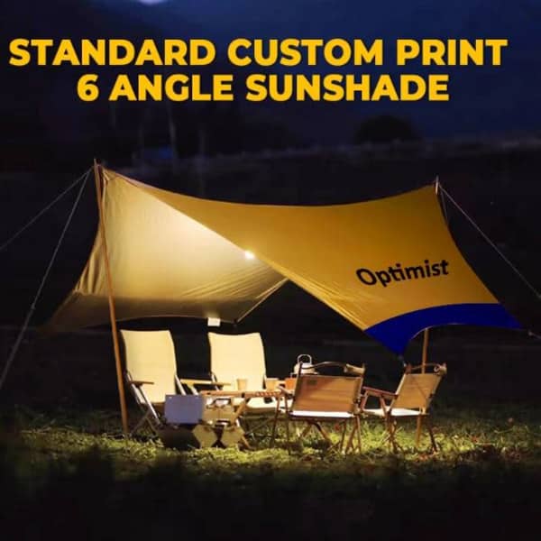 A yellow sunshade with blue branding and six angles, set up over outdoor seating and a table at night.