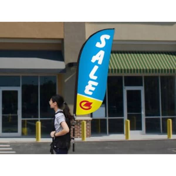 A small single-sided backpack wing banner in blue and yellow, attached to a person walking near a store.