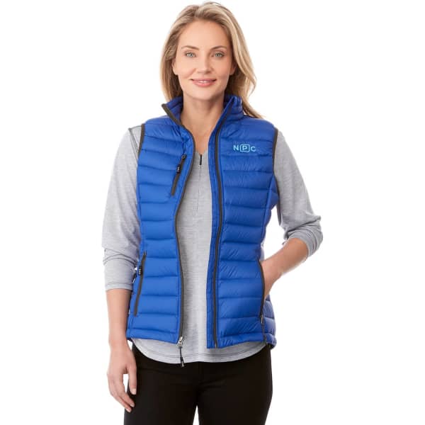 A woman in a blue lightweight down vest, with a grey top underneath, standing against a plain background.