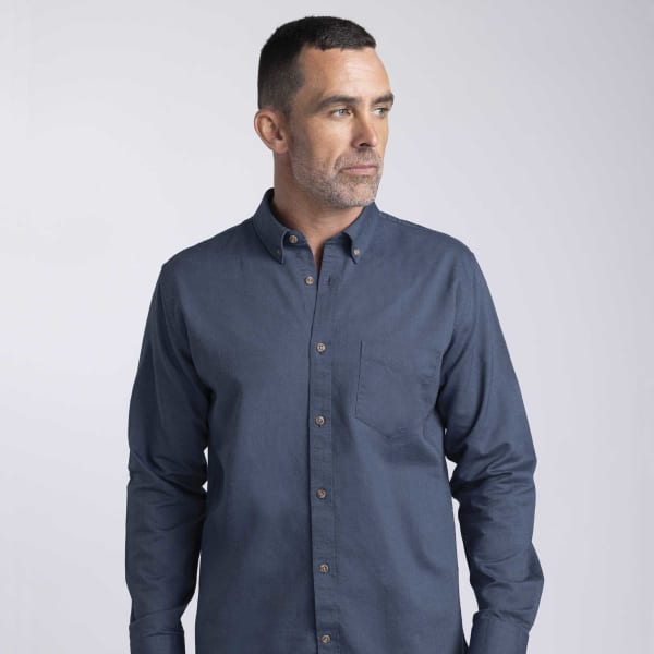 A man wearing a navy blue button-up shirt with a pocket and a logo. The shirt features a classic collar.