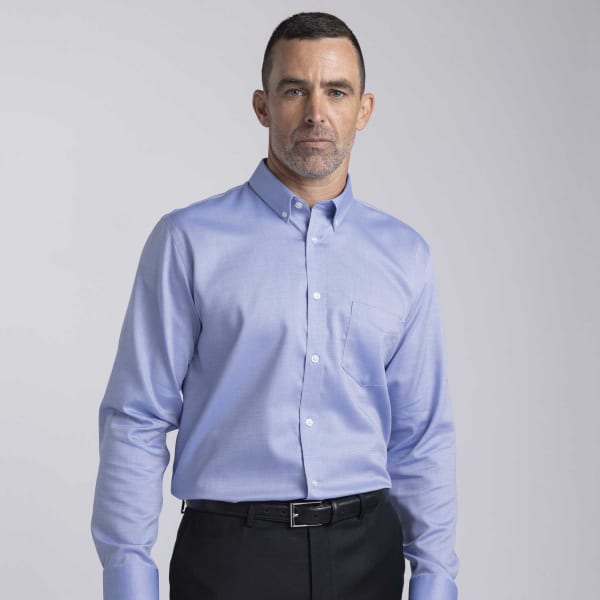 A formal button-up shirt in light blue, featuring a pocket and a collar, modelled by a man in dark trousers.