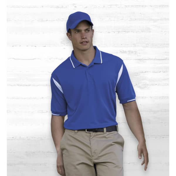 A blue polo shirt with white accents, worn by a model against a light wooden background. The model is also wearing a blue cap.